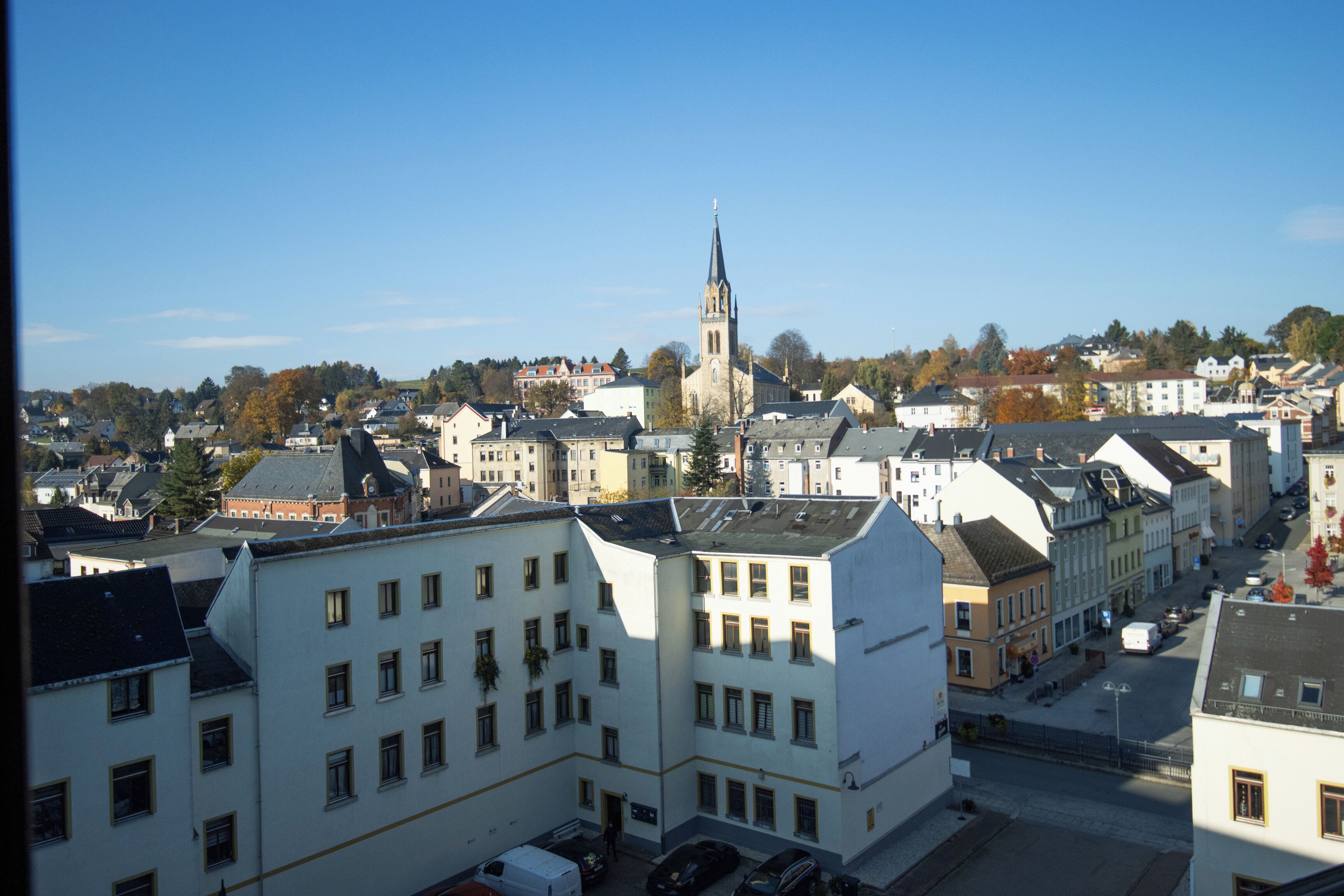 A cityscape with a prominent church tower, a mix of residential and commercial buildings, and a clear sky.