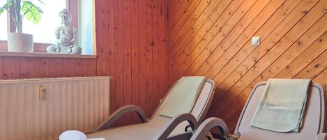 A room with wooden panel walls, two reclining chairs with towels, a potted plant, and a statue.