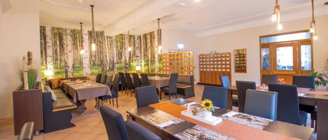 A spacious restaurant with high tables and chairs, a large mural of trees, and a modern design.