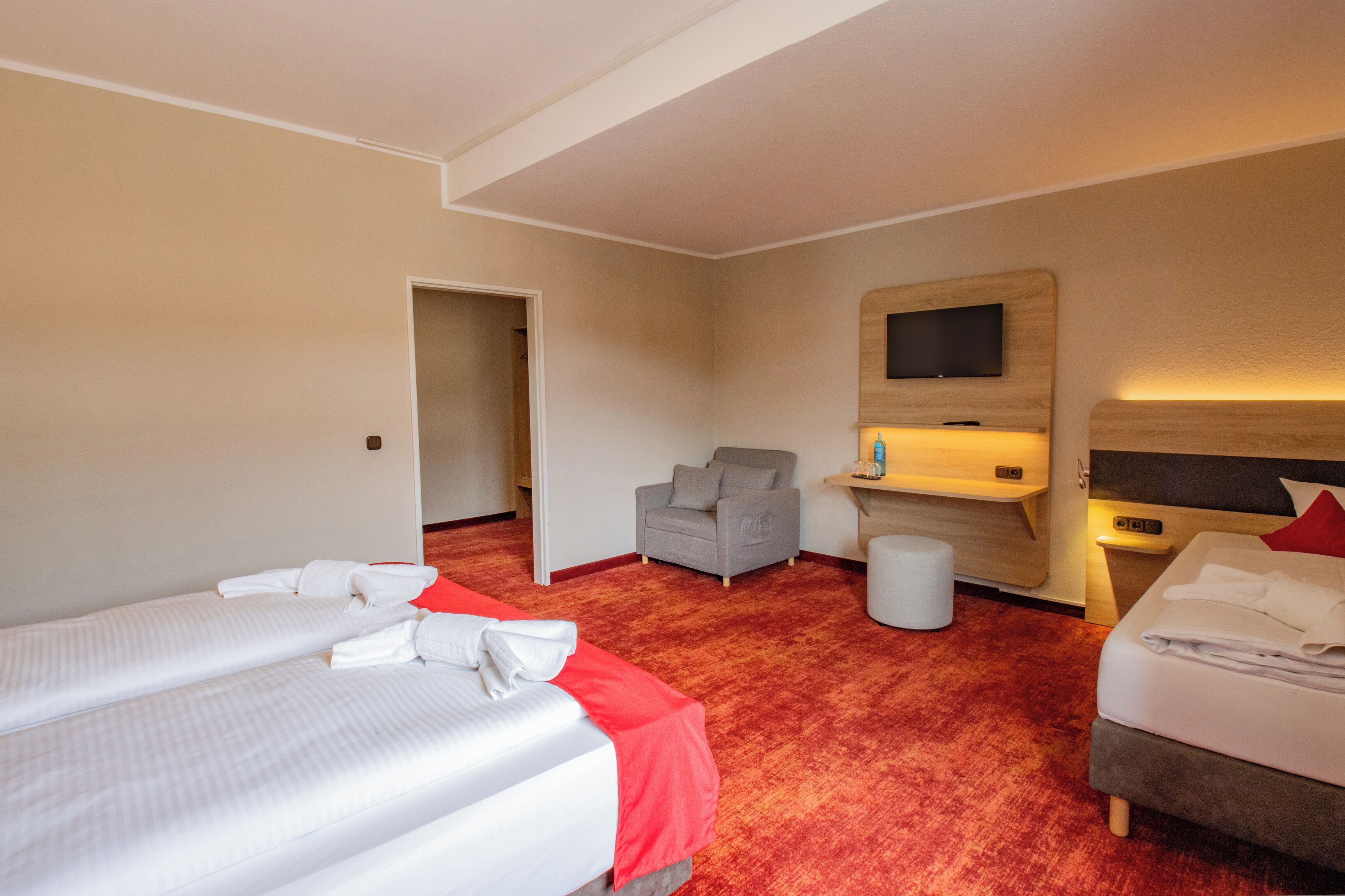 Ein Hotelzimmer mit zwei Betten, einem an der Wand montierten Fernseher, einem Sessel und einem kleinen Tisch.