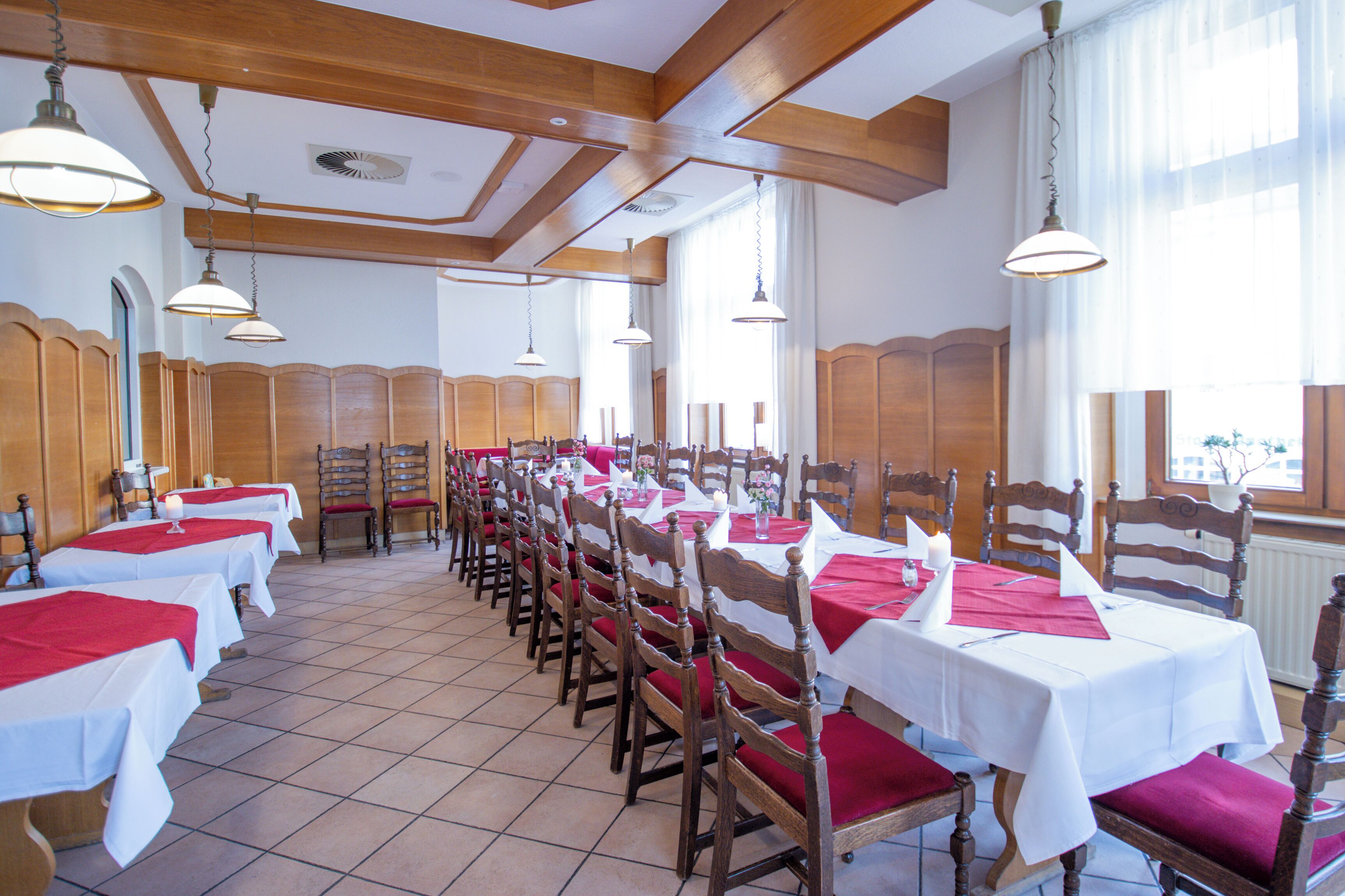 A dining area with multiple tables and chairs, wooden beams on the ceiling, and large windows.