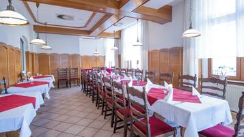 A dining area with multiple tables and chairs, wooden beams on the ceiling, and large windows.