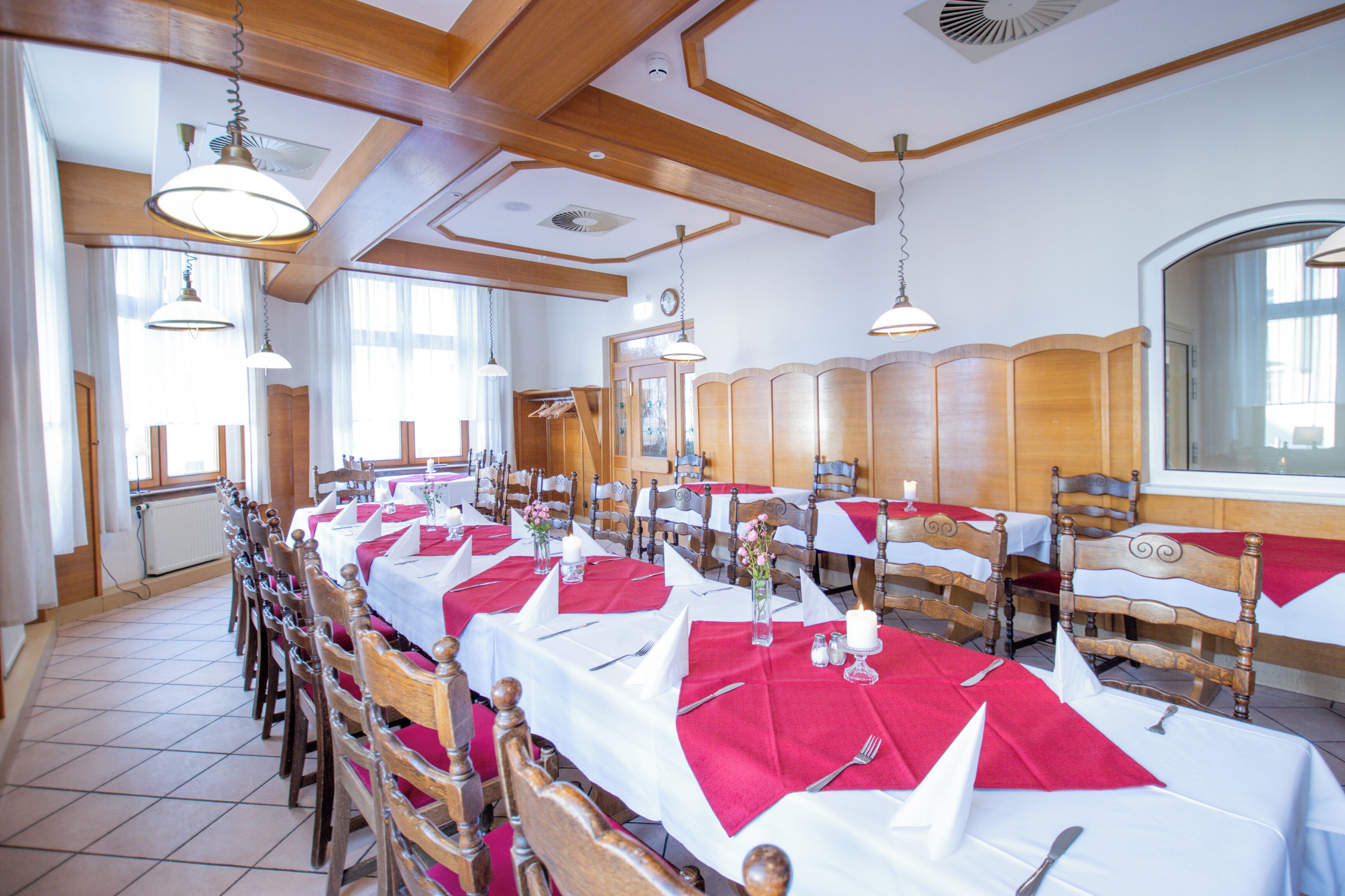 Un comedor con largas mesas dispuestas para muchos invitados, sillas de madera y lámparas colgantes.