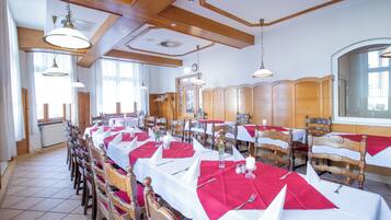 Un comedor con largas mesas dispuestas para muchos invitados, sillas de madera y lámparas colgantes.