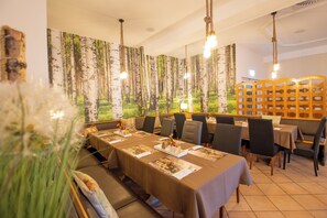 Un restaurante con mesas largas, sillas y una pared decorada con motivos forestales.