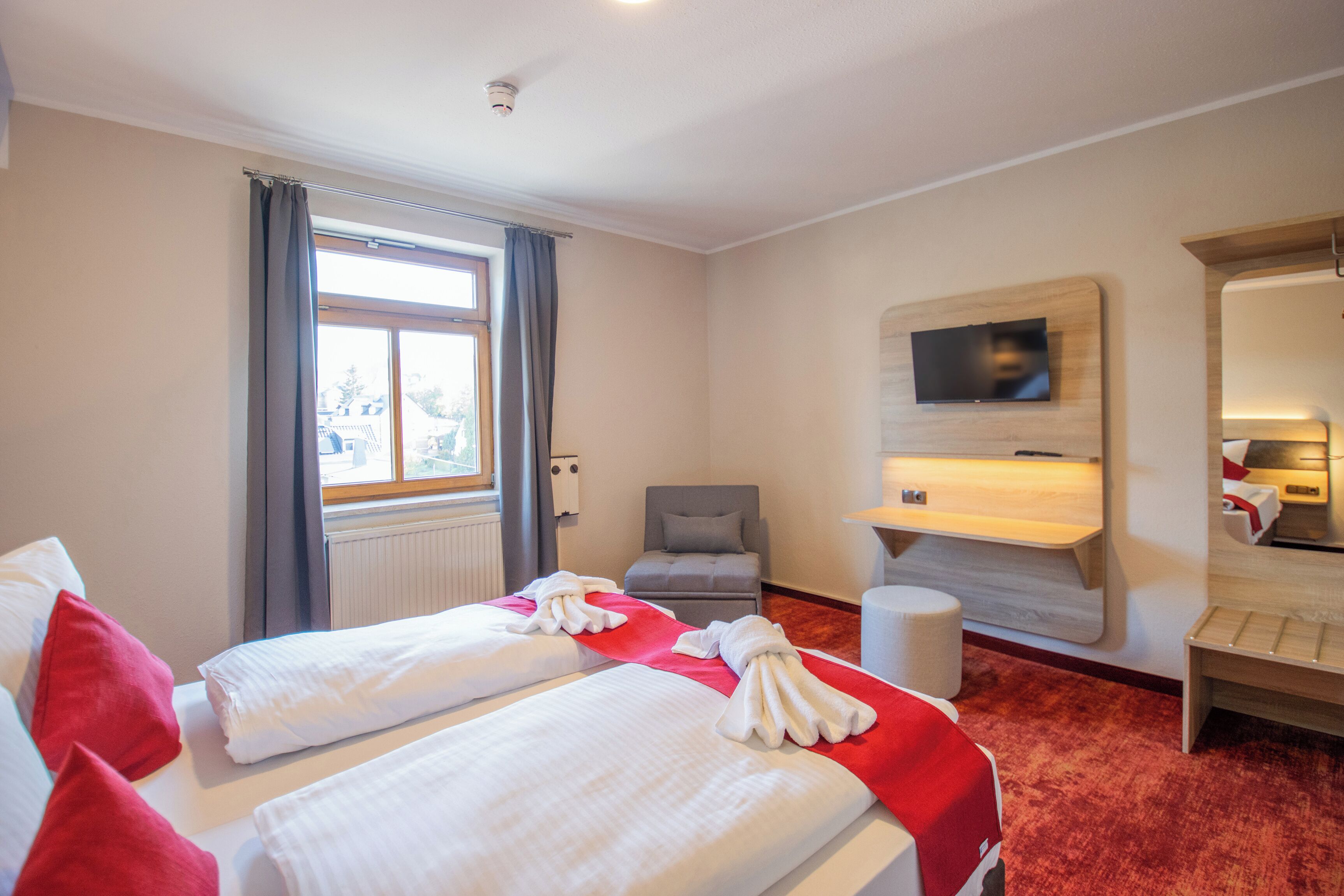 Ein Hotelzimmer mit zwei Betten, einem Fernseher, einem Schreibtisch und einem Sessel.