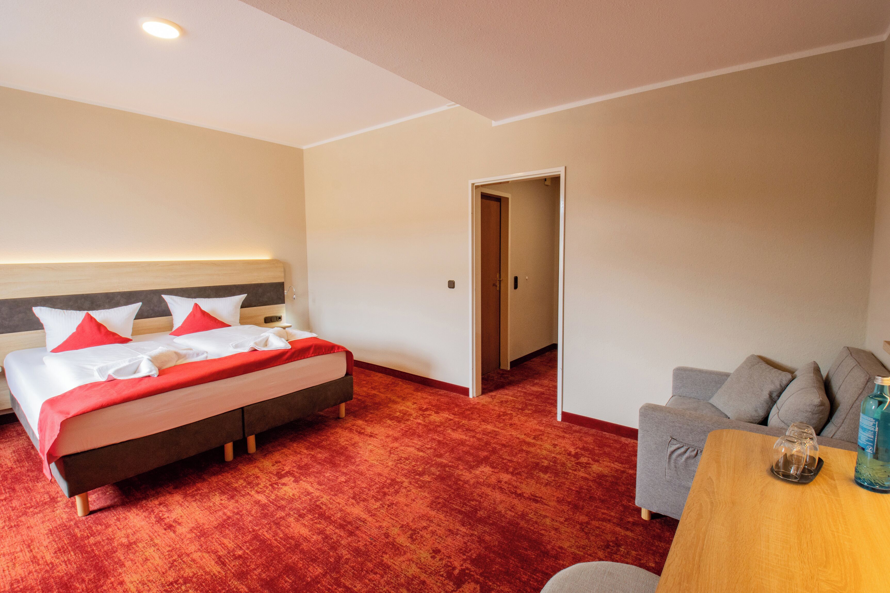 A hotel room with a bed, a sofa, a wooden table, and a door leading to another room.