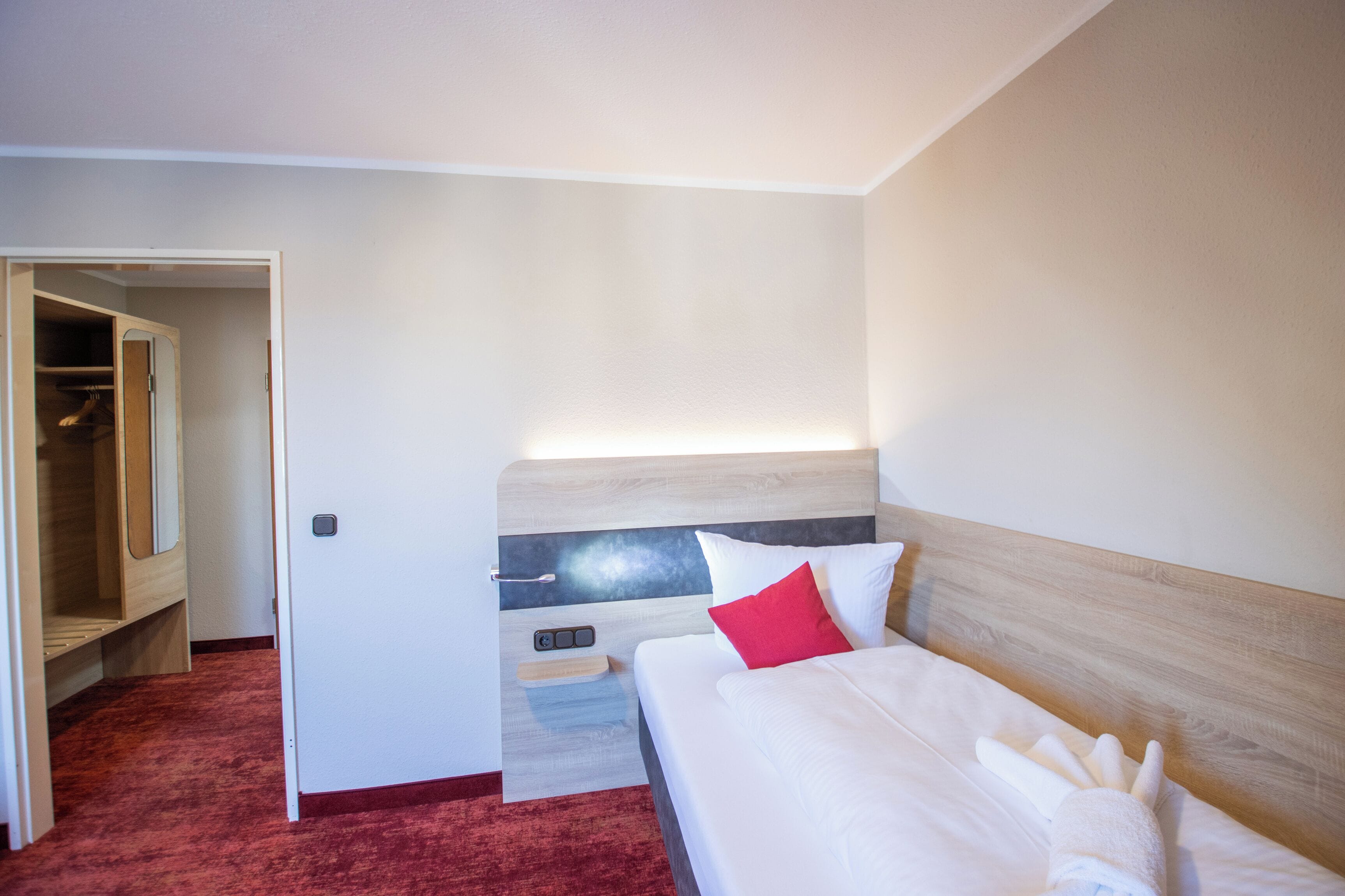 A hotel room with a bed, a nightstand, a mirror, and a closet.