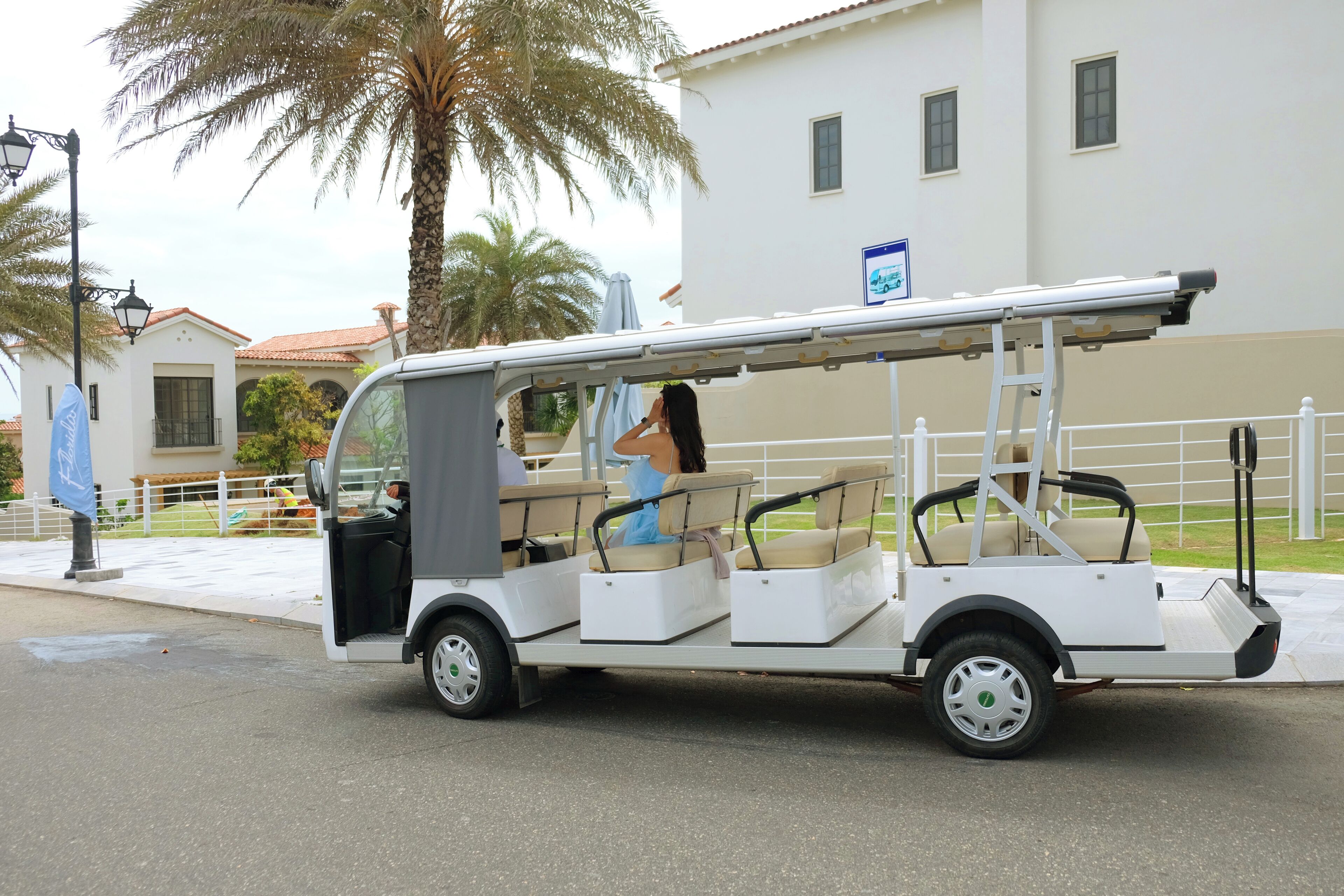 A white golf cart with three seats and a driver, parked on a street.