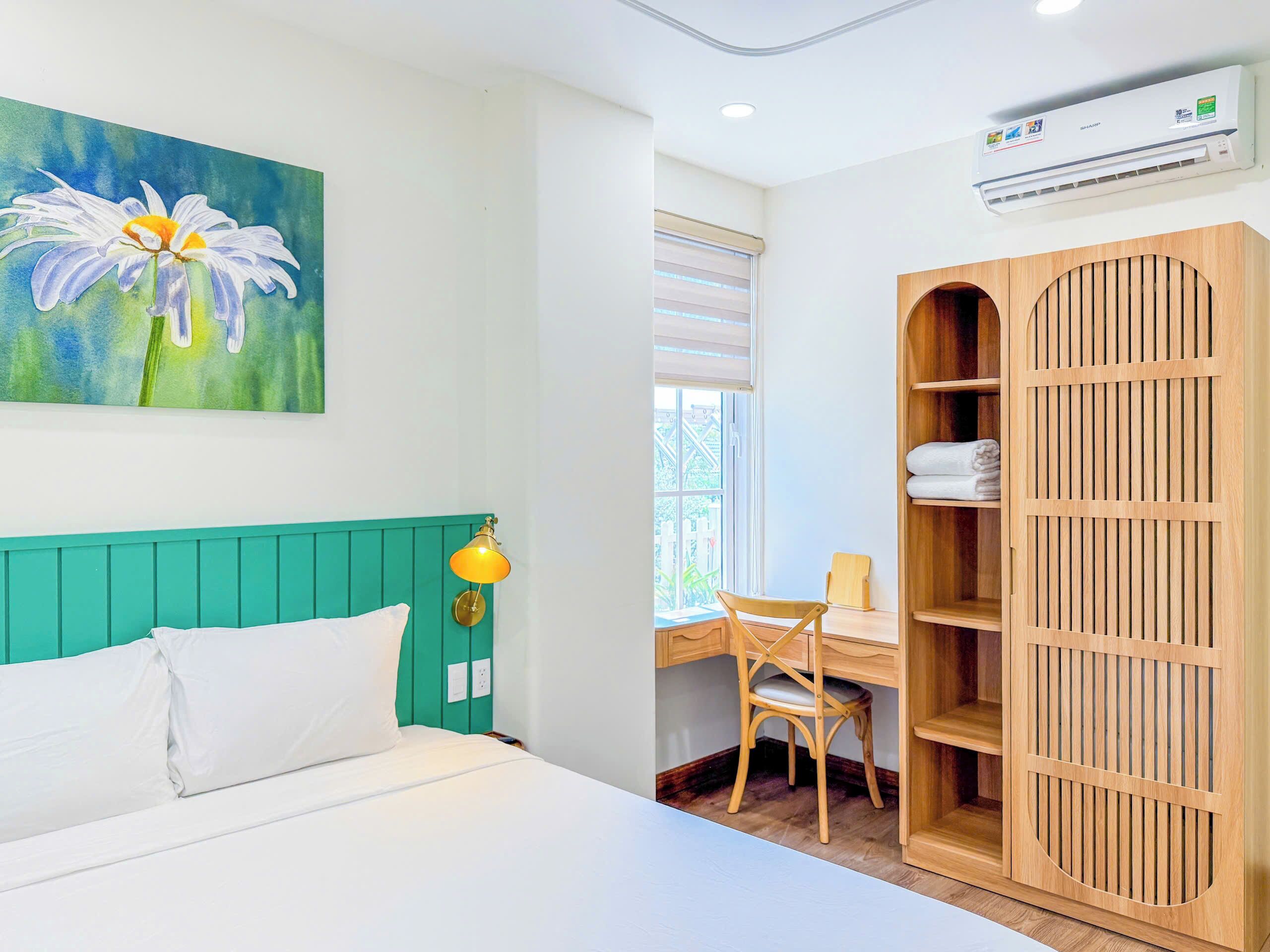 A room with a bed, a desk, a chair, a wardrobe, and a painting of a flower.