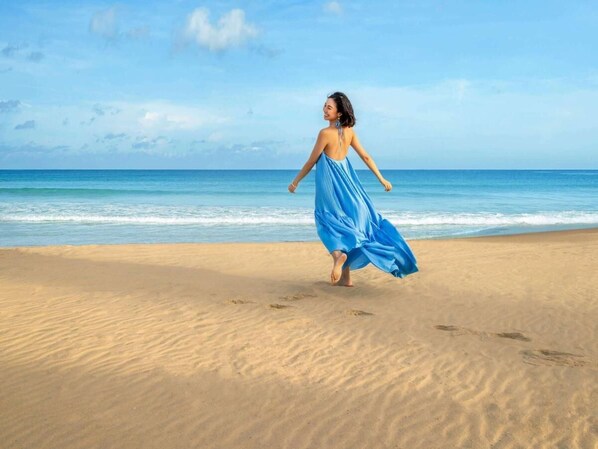 Une personne court sur une plage de sable, avec un ciel dégagé et une mer calme en arrière-plan.