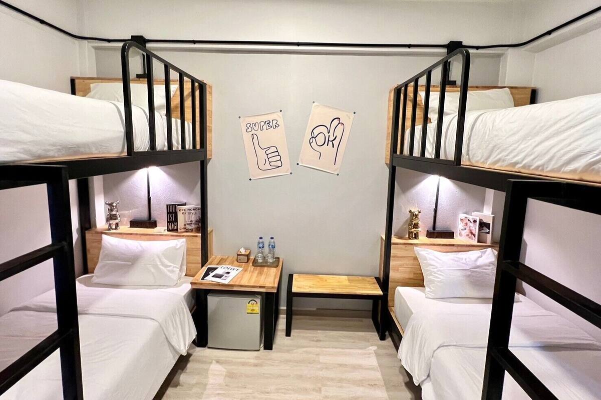 A dormitory room with bunk beds, a small table with a book and a bottle, and a wall with two signs.