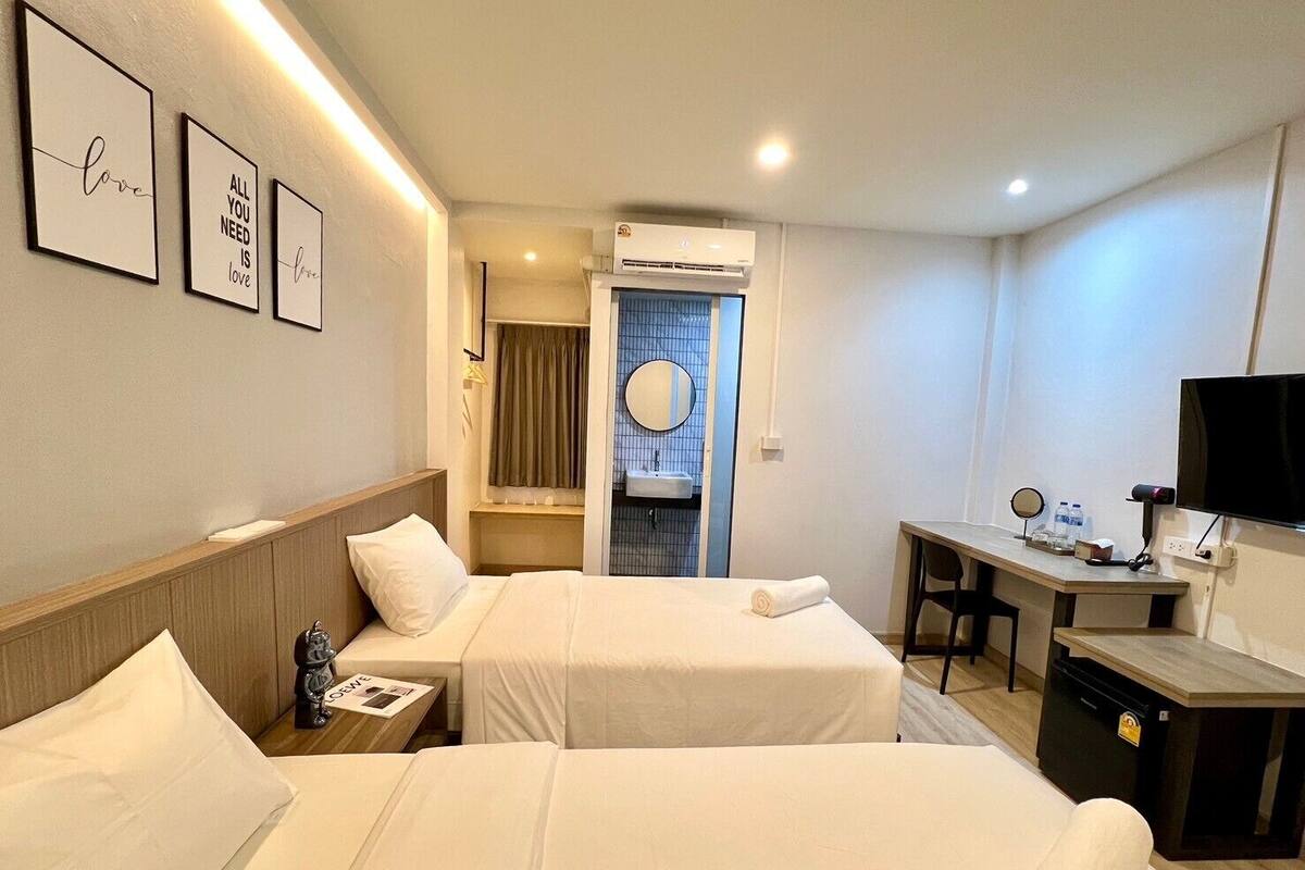 A hotel room with two beds, a desk, a TV, and a bathroom visible through a door.