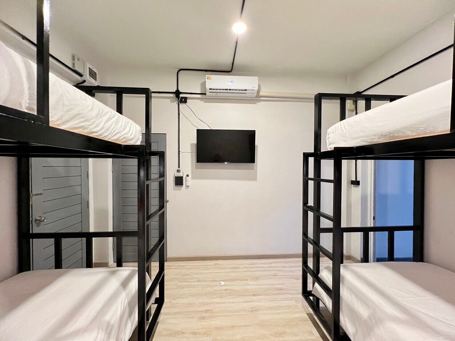 A dormitory room with bunk beds, a TV, an air conditioning unit, and a window with a view.