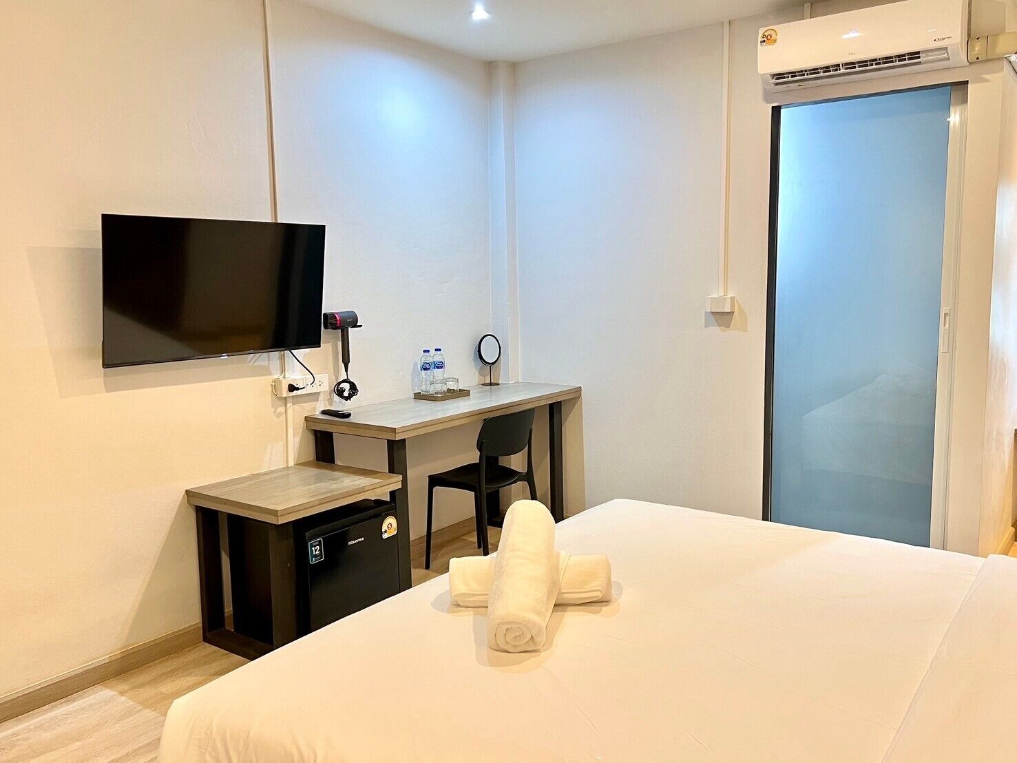 Habitación de hotel con cama, escritorio, silla, televisor, minibar y puerta corredera.