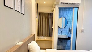 Hotelkamer met twee bedden, een houten hoofdbord, een nachtkastje met lamp, een ingelijst schilderij aan de muur, en een badkamer met spiegel en wastafel.