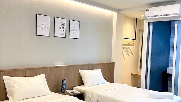 Een hotelkamer met twee bedden, een nachtkastje, een wandairconditioner en drie ingelijste motiverende citaten.