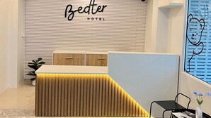 Een hotel receptie met een modern design, inclusief een receptiebalie, een wandbord, een beveiligingscamera en een raam met zonwering.