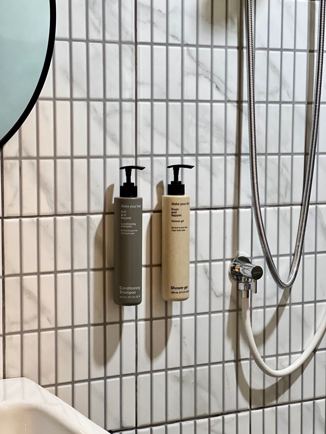 A bathroom with a shower, two bottles of shampoo, and a handheld showerhead.
