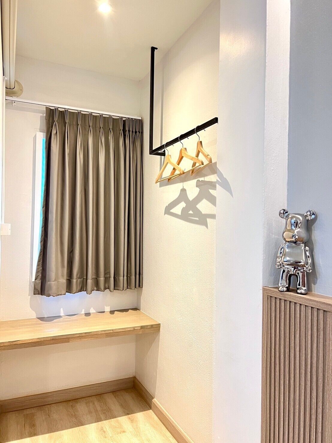 Quarto de canto com janela, um banco de madeira, um radiador e um cabide fixado na parede.