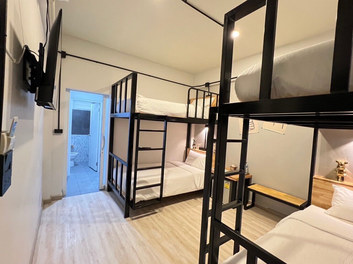 A bunk bed room with a TV mounted on the wall, a wooden floor, and a door leading to a bathroom.