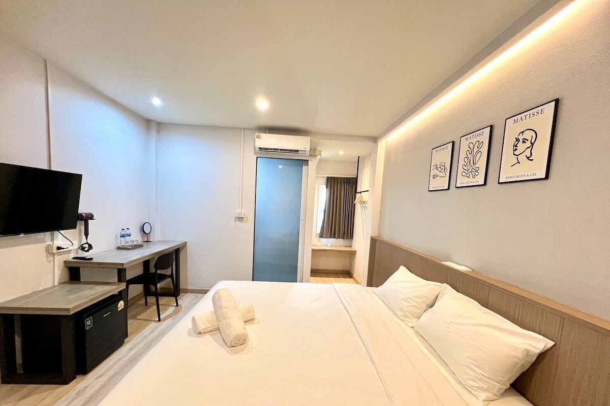 A hotel room with a bed, a desk, a TV, and artwork on the wall.