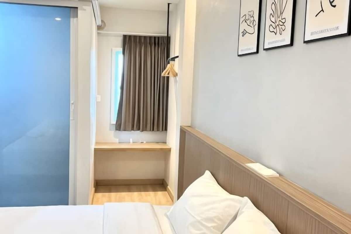 A hotel room with a bed, a wooden headboard, a small desk, a mirror, and a window with curtains.