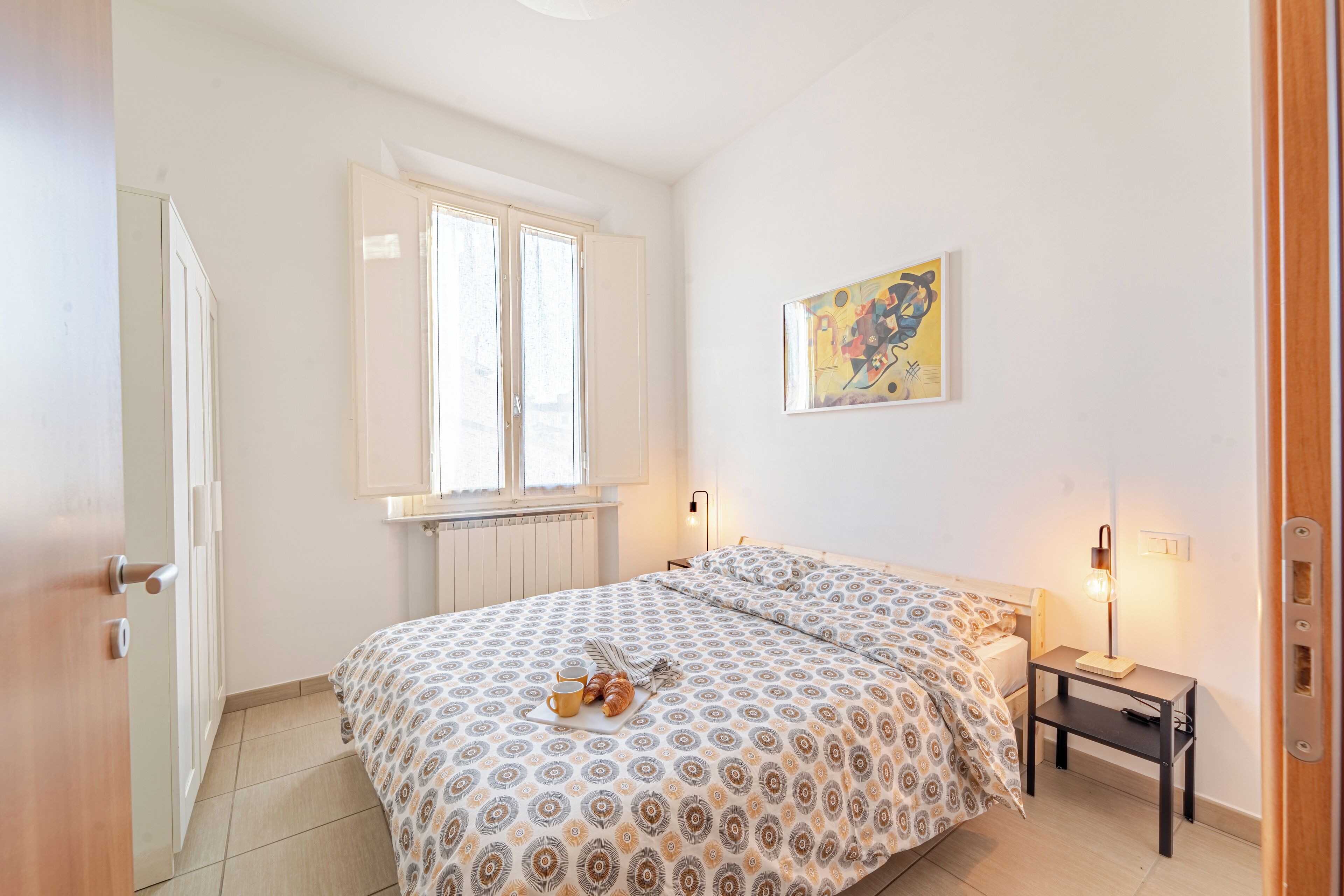 Un dormitorio con cama, mesita de noche, lámpara y ventana.