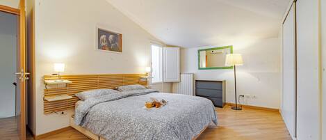 A bedroom with a bed, bedside lamps, a painting, a mirror, and a fireplace.