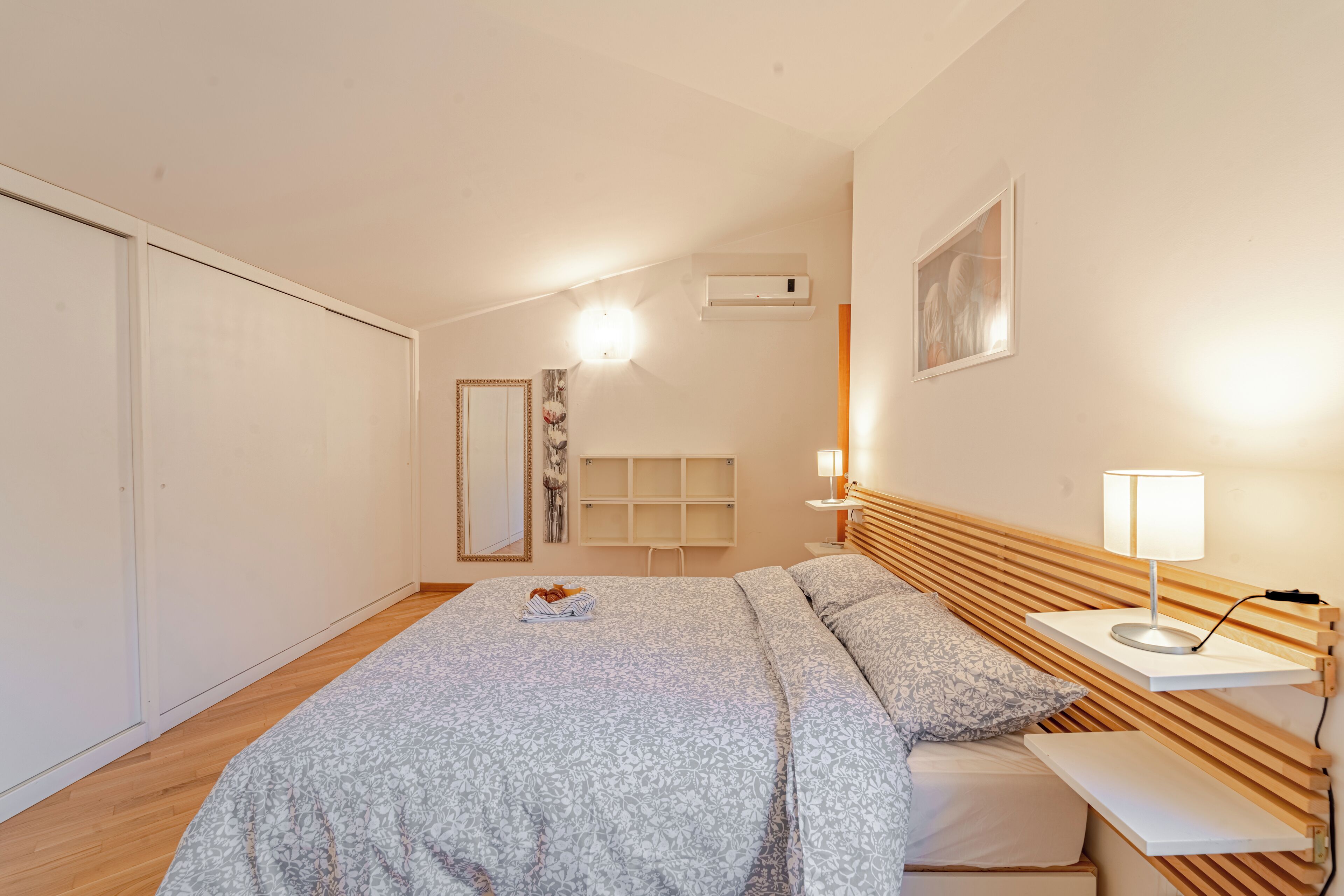 Un dormitorio con cama, mesita de noche, lámpara y estante en la pared.