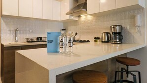 Une cuisine moderne avec des meubles blancs, un plan de travail blanc, une machine à café et deux bouteilles d’eau.