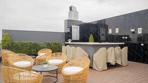 Un bar situé sur le toit, avec des chaises en osier et une table, un mur en marbre noir et une enseigne sur laquelle on peut lire « ARTLINE ».