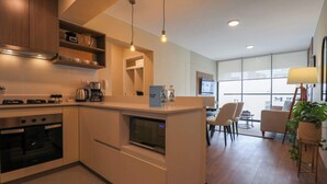 Una cocina moderna con electrodomésticos integrados, un comedor con sillas y un amplio ventanal que proporciona luz natural.