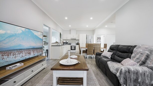 A modern living room with a flat-screen TV, a black leather sofa, and a dining area with wicker chairs.