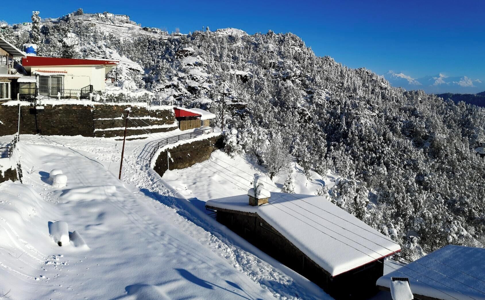 A snow-covered mountain landscape with buildings, including a red-roofed structure and a stone wall.