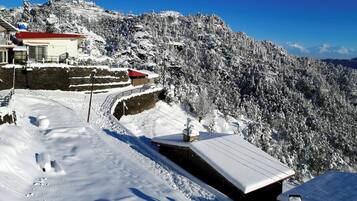 A snow-covered mountain landscape with buildings, including a red-roofed structure and a stone wall.