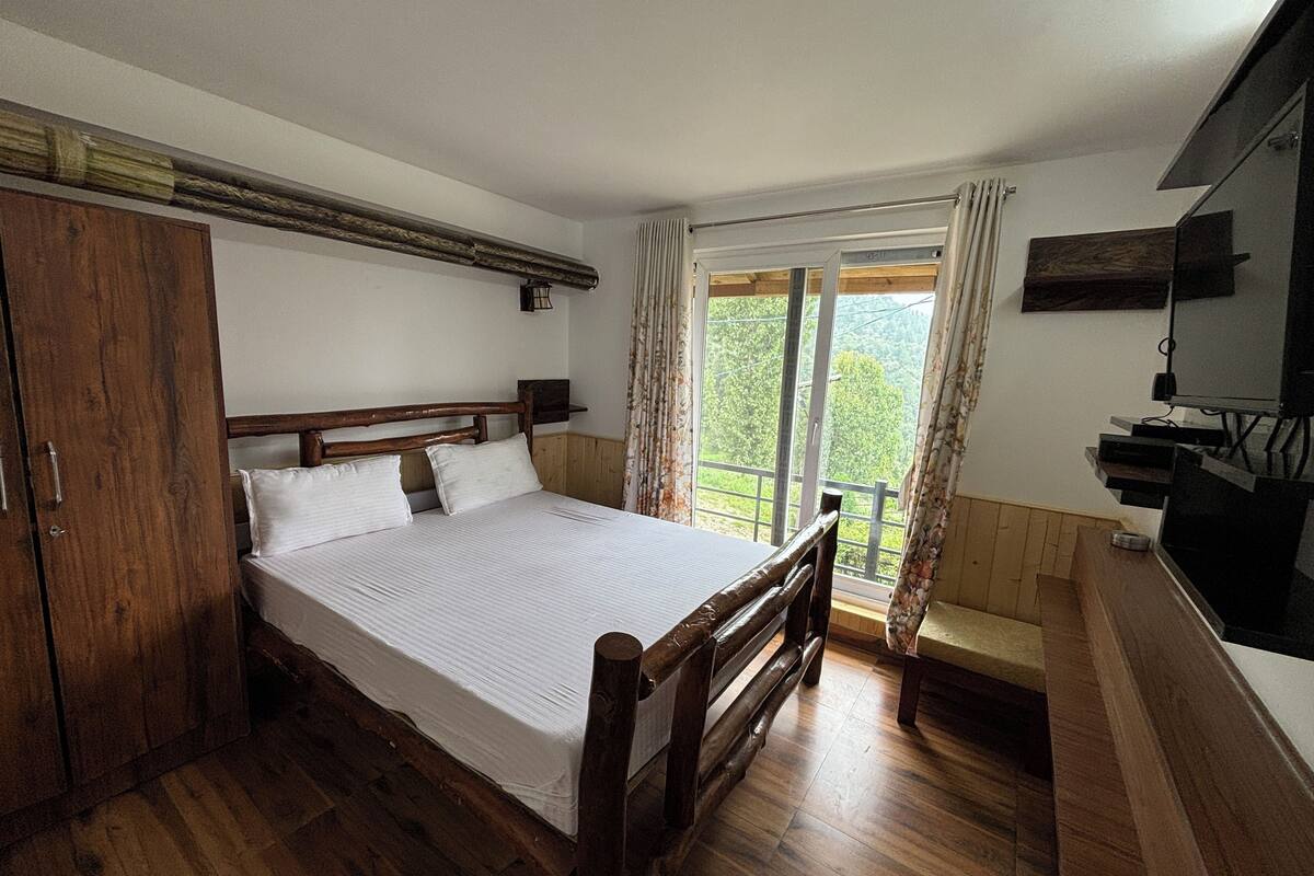 Une chambre à coucher avec un lit en bois, une armoire, un téléviseur et un balcon agrémenté de rideaux.