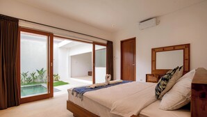 Un dormitorio con una cama grande, cabecera de madera, mesita de noche, un tocador, un espejo amplio y una puerta corrediza de vidrio que da a un balcón con piscina.