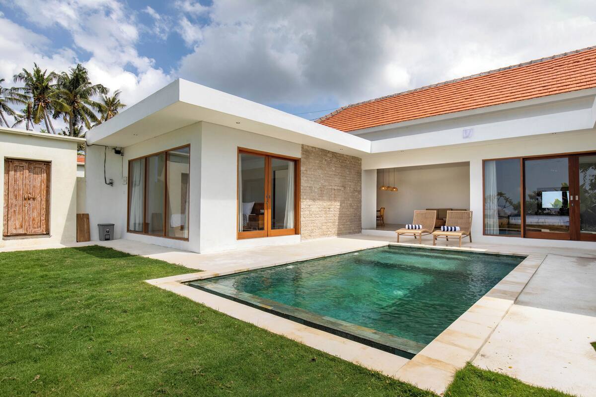 A modern house with a swimming pool, large windows, and a well-maintained lawn.