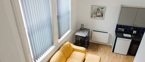 A modern apartment with a wooden staircase, a yellow sofa, a small kitchen, and large windows with blinds.