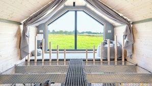 A cozy, triangular room with a large window, a metal grate floor, and a view of a green field. - Domek Freedom Sun & Snow (gmina Wolin)