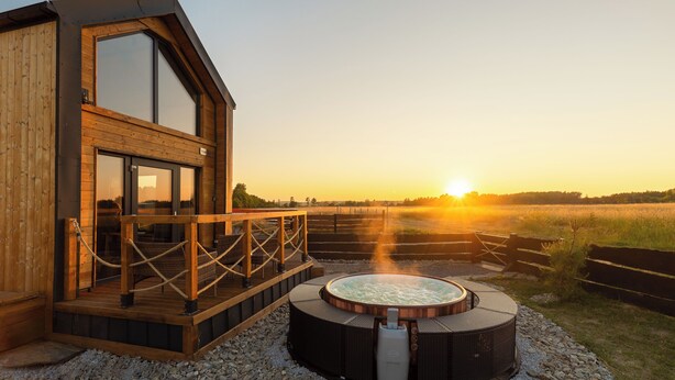 A wooden cabin with a hot tub and a deck overlooking a field. - Domek Freedom Sun & Snow (gmina Wolin)