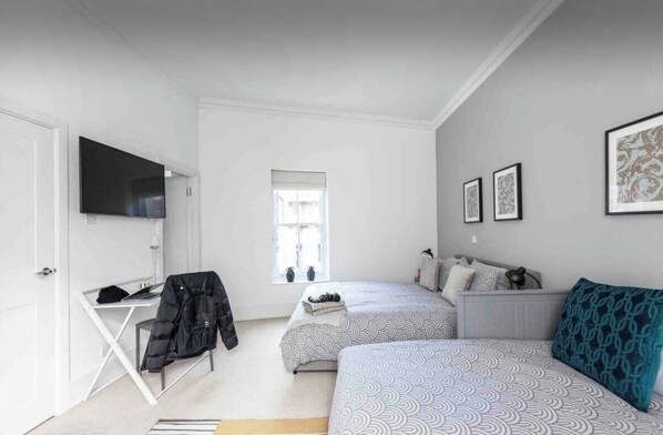 A bedroom with two beds, a desk, a TV, and a window.