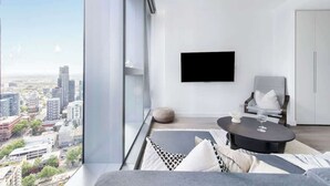 Ein modernes Wohnzimmer mit Blick auf die Stadt, einem Flachbildfernseher, einem grauen Sofa, einem runden Couchtisch und einem grauen Sessel.