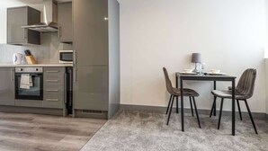 A modern kitchen with stainless steel appliances, a dining area with two chairs and a table, and a grey carpet. - Bright 1 Bed Apartment in Yeadon (Yeadon)