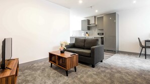 A modern living room with a grey sofa, a wooden coffee table, a TV, and a kitchen in the background. - Bright 1 Bed Apartment in Yeadon (Yeadon)