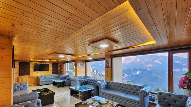 A spacious living area with wooden ceilings and large windows offering a mountain view. - Hotel Snow Lotus (Shimla)