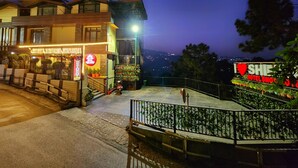 A hotel with a balcony, a sign for a restaurant, and a view of the city at night. - Hotel Snow Lotus (Shimla)