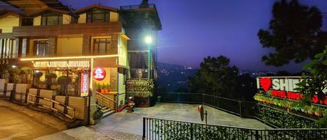 A hotel with a balcony, a sign for a restaurant, and a view of the city at night.