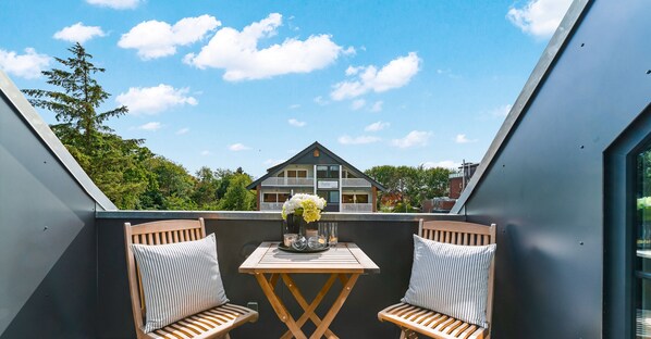 A balcony with two wooden chairs, a small table, and a vase of flowers. - Relax and unwind in the heart of St. Peter-Ording (Sankt Peter-Ording)